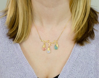 May include: A gold necklace with a delicate branch design and three teardrop-shaped gemstones in pink, white, and blue.