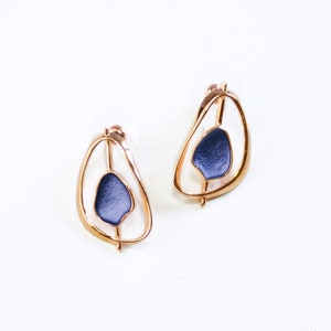 Stud Earrings with an open Pear shape rose gold plated pendant with a floating textured disc center painted in blue enamel on a white background