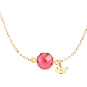 May include: A gold chain necklace with a pink gemstone pendant and a small gold bird charm with the letter 'A' engraved on it.
