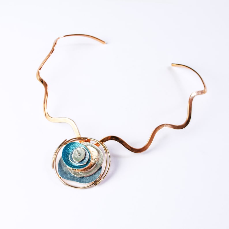 Necklace with copper wavy neck ring and a round pendant made of 6 rose gold plated overlapping abstract textured discs painted in teal, blue, and gray enamel against a white background