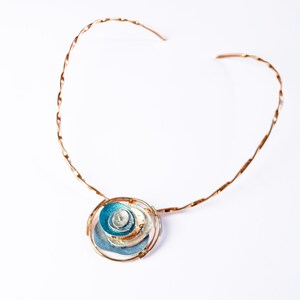 Necklace with copper flat twisted neck ring and a round pendant made of 6 rose gold plated overlapping abstract textured discs painted in teal, blue, and gray enamel against a white background