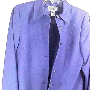 Puede incluir: Una camisa abotonada azul bígaro con mangas largas. La camisa tiene cuello y una etiqueta que dice "Pendleton". La camisa está colgada en una percha blanca.