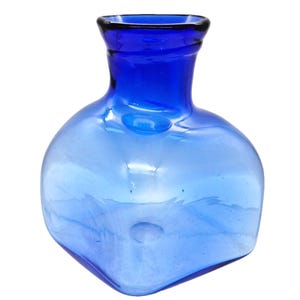 Puede incluir: Un jarrón de vidrio azul con base cuadrada y cuerpo redondeado. El jarrón hace la transición de un azul más claro en la base a un azul más oscuro en el cuello. La abertura es de color azul oscuro.