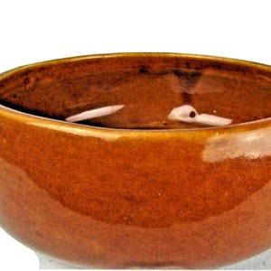 May include: A brown ceramic bowl with two small handles. The bowl has a glossy finish and a rounded shape. The interior is a darker shade of brown. This bowl is suitable for serving soups or stews, with a capacity of approximately 1 liter.