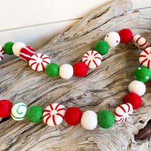 May include: A festive garland made of felt balls in red, white, and green. The balls are decorated with peppermint designs and white polka dots.