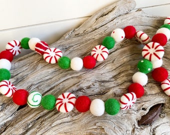 May include: A festive garland made of felt balls in red, white, and green. The balls are decorated with peppermint designs and white polka dots.