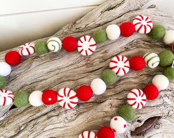 May include: A festive garland made of felt balls in red, white, and green. The balls are decorated with peppermint candy designs.