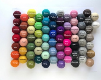 May include: A collection of 60 felt balls in various colors, including red, blue, green, yellow, orange, purple, pink, brown, and grey. The balls are arranged in rows and columns on a white surface.
