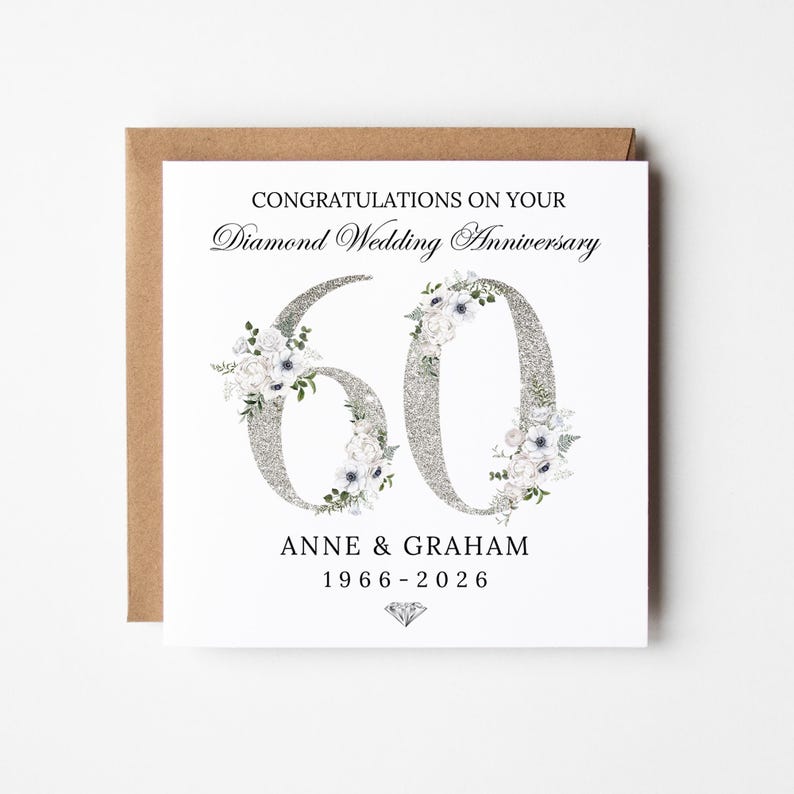 May include: A square greeting card with a brown envelope featuring the text CONGRATULATIONS ON YOUR Diamond Wedding Anniversary. The number 60 is displayed in a large silver glitter font decorated with white floral illustrations, ANNE & GRAHAM, 1966-2026, and a small diamond icon.