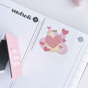 May include: A pink and white planner with the words "vendredi-28" and "dimanche-30" written on it. A pear sticker with a pink heart is on the page. Pink and white washi tape is on the right side of the image.