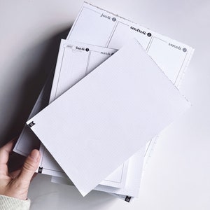 May include: A stack of white weekly planner pages with black text and dotted lines. The pages are labelled with the days of the week in French: lundi, mardi, mercredi, jeudi, vendredi, samedi.
