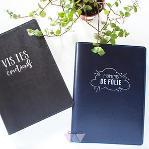 Peut inclure: Deux journaux en cuir noir avec du texte blanc. Un journal dit "Vis tes emotions" et l'autre dit "Moments de folie" dans un nuage.