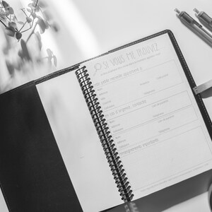 Peut inclure: Un journal reli&eacute; en cuir noir avec une reliure spirale. Le journal est ouvert &agrave; une page avec le titre "Si vous me trouvez" et une section pour les coordonn&eacute;es. Le journal est sur une surface blanche avec une plante et deux stylos.
