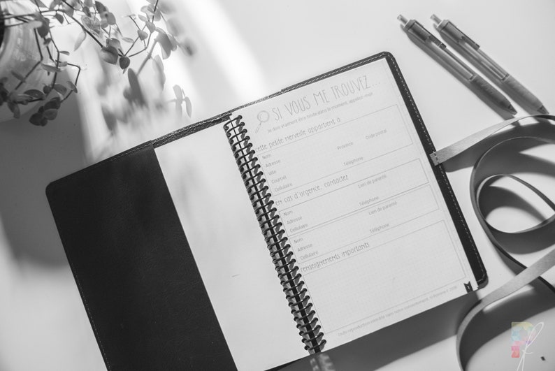 Peut inclure: Un journal reli&eacute; en cuir noir avec une reliure spirale. Le journal est ouvert &agrave; une page avec le titre "Si vous me trouvez" et une section pour les coordonn&eacute;es. Le journal est sur une surface blanche avec une plante et deux stylos.