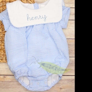 May include: A blue and white gingham baby onesie with a white bib collar and the name "henry" embroidered on the collar.