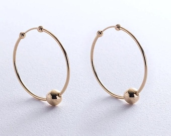 May include: A pair of gold hoop earrings, each featuring a single polished gold bead threaded onto the thin circular wire. The earrings have a simple clasp mechanism at the top of the hoop. The image includes a green rectangular label with the text Fast shipping.