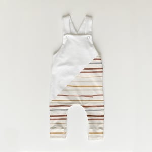 May include: White baby overalls with a diagonal stripe pattern in shades of brown, beige, and gray. The stripes are painted on the fabric.