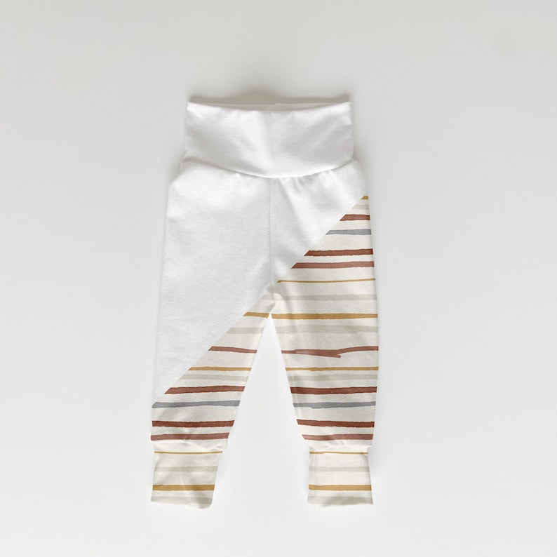 May include: White baby leggings with a diagonal stripe pattern in shades of brown, beige, and gray. The stripes are on one leg and the other leg is solid white.
