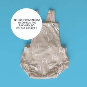 May include: A beige baby onesie with a white rainbow pattern. The onesie has a snap closure at the crotch and adjustable straps. Instructions on how to change the background color are included.