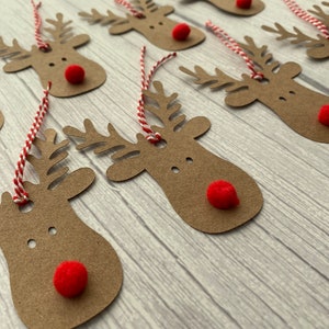 May include: A set of brown paper reindeer gift tags with red pom-poms for noses and red and white twine.