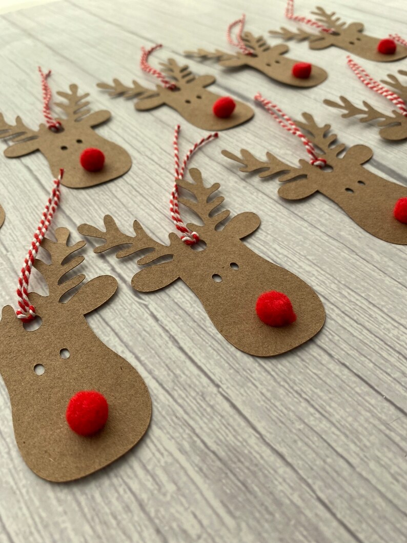 May include: A set of brown paper reindeer gift tags with red pom-poms for noses and red and white twine.
