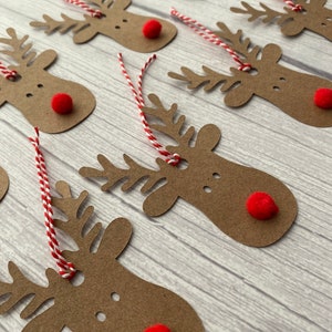 May include: A set of brown paper reindeer gift tags with red pom-poms for noses and red and white twine.
