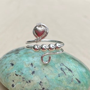 May include: A silver ring with a heart charm and four silver beads. The ring is on a green and white stone.