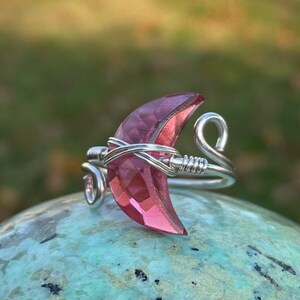 May include: A silver wire wrapped ring with a pink crescent moon shaped crystal.