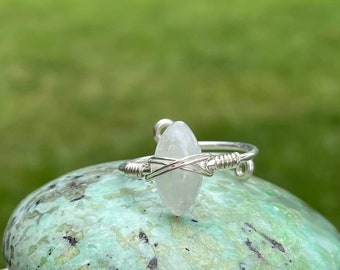 May include: A silver wire wrapped ring featuring a clear, oval-shaped gemstone.