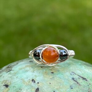 May include: A silver wire wrapped ring with an orange gemstone and two black hematite beads.