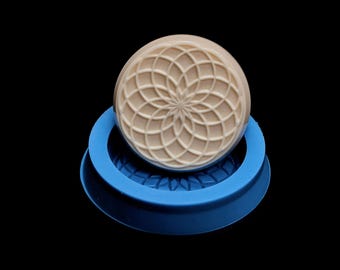 May include: A beige soap bar with a geometric pattern sits in a blue silicone mold. The mold has a raised design around the edge.