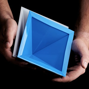 May include: A blue square-shaped bowl with a white rim, held in two hands. The bowl is made of a smooth, glossy material.