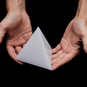 May include: A white pyramid shape held in two open hands against a black background.