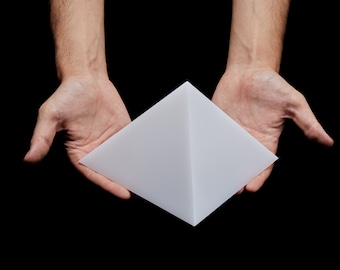 May include: A white pyramid-shaped object held in two hands against a black background.