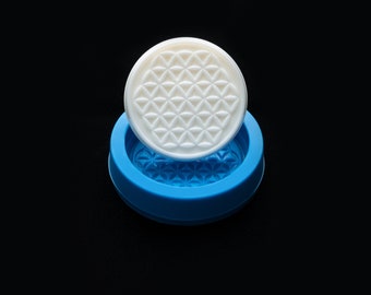 May include: A white silicone mold with a flower of life design. The mold is sitting on a blue silicone base.