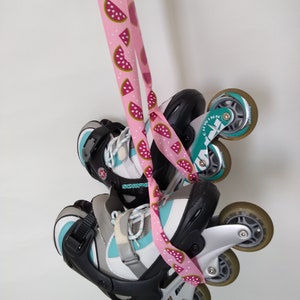 May include: A pair of black and teal inline skates with white wheels and a pink watermelon-patterned strap. The skates are hanging from the strap.