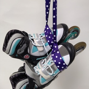 May include: A pair of teal and gray rollerblades with white laces and a purple polka dot ribbon tied around them.
