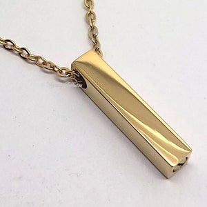 May include: A gold bar pendant necklace with a delicate chain. The pendant is a simple, rectangular shape with a smooth, polished finish.