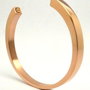 May include: A rose gold bangle bracelet with a screw closure.