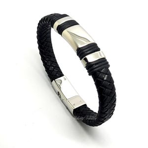 Op de afbeelding: Een zwarte leren armband met een zilveren metalen sluiting en een gevlochten ontwerp.