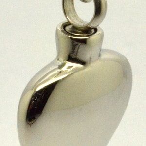 May include: A silver heart-shaped cremation pendant with a chain. The pendant has a screw-on lid for holding ashes.