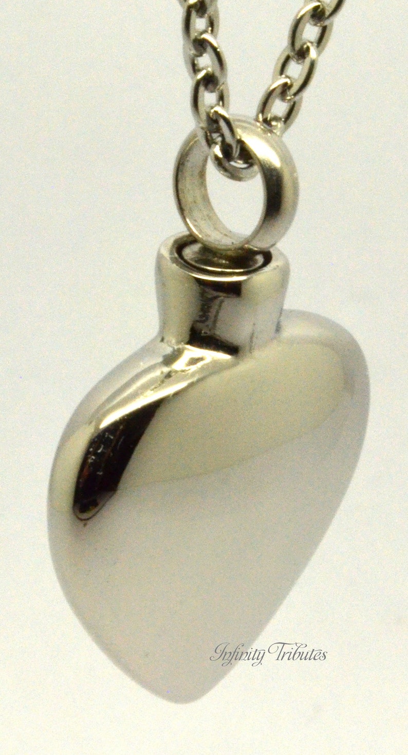 May include: A silver heart-shaped cremation pendant with a chain. The pendant has a screw-on lid for holding ashes.
