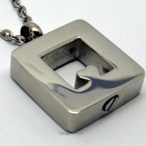 Può includere: Collana con ciondolo quadrato in argento con un ritaglio a forma di cuore. Il ciondolo ha una piccola apertura sul lato per aggiungere ceneri o altri ricordi.