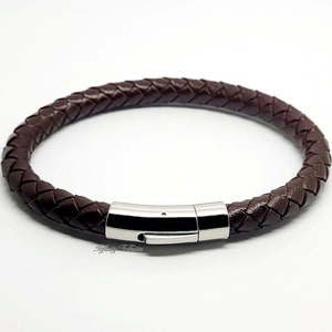 Puede incluir: Una pulsera trenzada de cuero marrón con un cierre de acero inoxidable. La pulsera es circular y parece estar hecha de hebras de cuero trenzado. El cierre es de color plateado brillante.