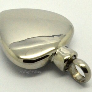 May include: A silver heart-shaped cremation urn pendant with a screw-on lid and a small loop for attaching to a chain.