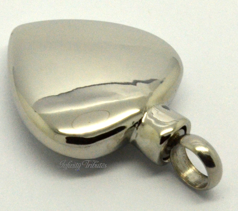 May include: A silver heart-shaped cremation urn pendant with a screw-on lid and a small loop for attaching to a chain.