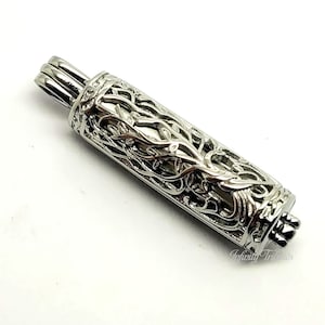 May include: Silver tone metal pendant with an intricate design of a tree with branches and leaves. The pendant is cylindrical and has a hinged lid.