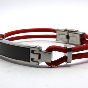 Peut inclure: Un bracelet en cuir rouge avec une fermeture en acier inoxydable et une plaque rectangulaire noire. La plaque a une surface lisse et est vide.