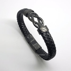 May include: Black braided leather bracelet with a stainless steel clasp and a decorative knot design. The bracelet features a woven leather band and a secure clasp. The knot design adds a unique touch to this accessory.