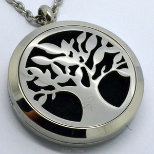 Op de afbeelding: Een zilveren ketting met een hanger in de vorm van een levensboom. De hanger is rond en heeft een zwarte achtergrond met een zilveren boomuitsparing. De ketting is gemaakt van een zilveren ketting.